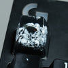 A close-up view of a black resin keycap featuring a detailed design of skulls and a raven's eye.