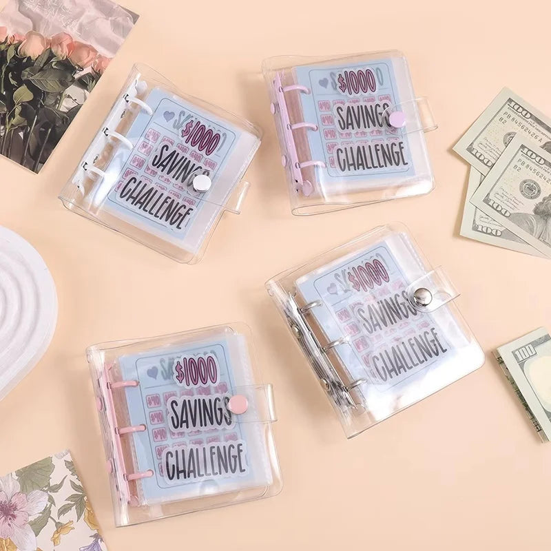 Eine Sammlung klarer Plastik-Sparhefte mit der Aufschrift 1000 Spar-Challenge, mit rosa und blauen Akzenten.