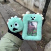 A hand holds a light green plush photocard holder with a clear window displaying a photo.
