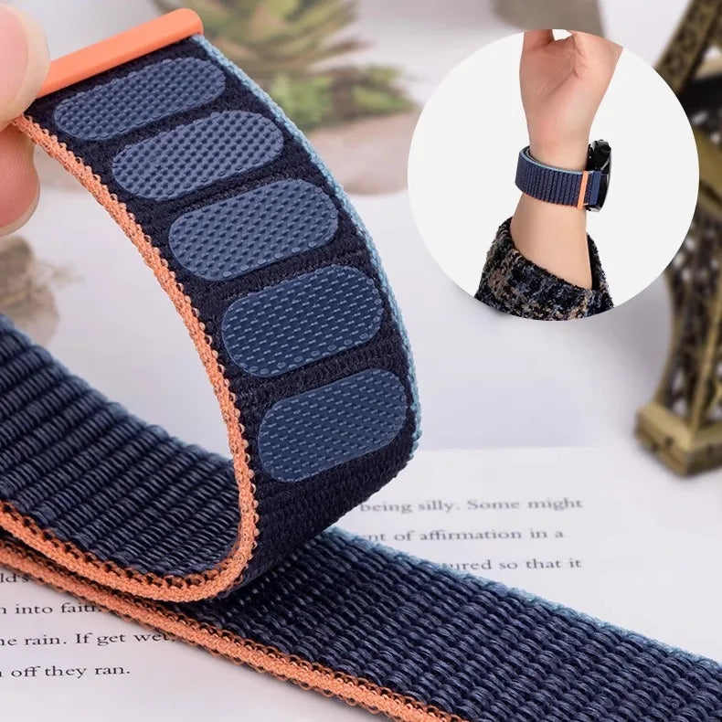 A close-up of a navy blue nylon watch strap with an orange edge, showing its texture and adjustable loop.