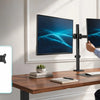 A man is using a heavy duty dual monitor desk mount to position two computer monitors on a wooden desk.