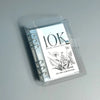A clear plastic binder showing a monthly savings challenge with floral illustrations and the name Cin Girl Cashi Stufeer