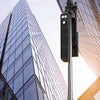 A black portable Bluetooth selfie stick tripod with a fill light and remote is shown against a modern glass building.