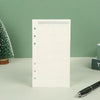 Un cuaderno de hojas sueltas blanco con diseño de cuadrícula y páginas perforadas, junto a un bolígrafo negro.