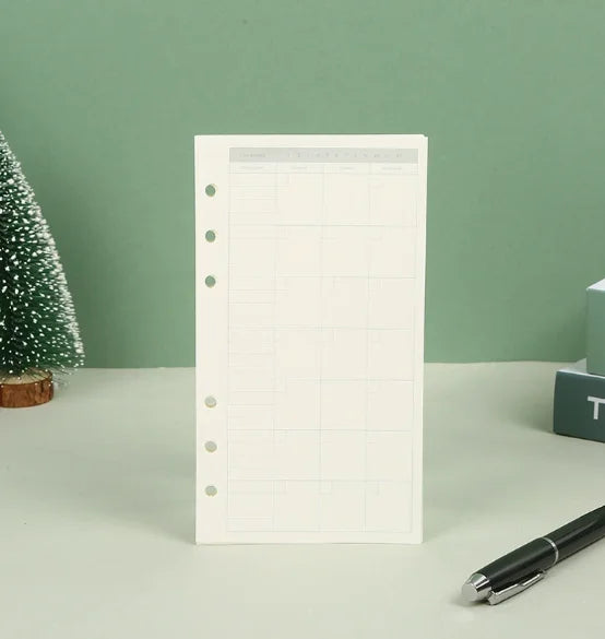 Un cuaderno de hojas sueltas blanco con diseño de cuadrícula y páginas perforadas, junto a un bolígrafo negro.