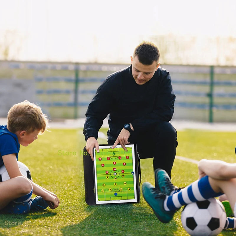 A man is using a foldable magnetic soccer coaching board with markers on a green field.