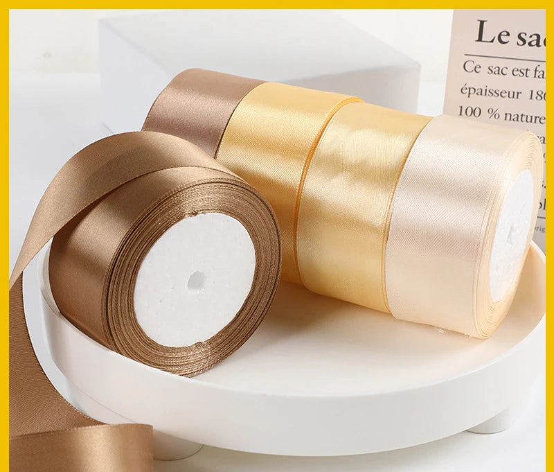 Rolls of satin ribbon in beige and gold colors displayed on a white surface.