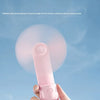 A hand holds a pink portable foldable rabbit mini fan against a light blue sky.