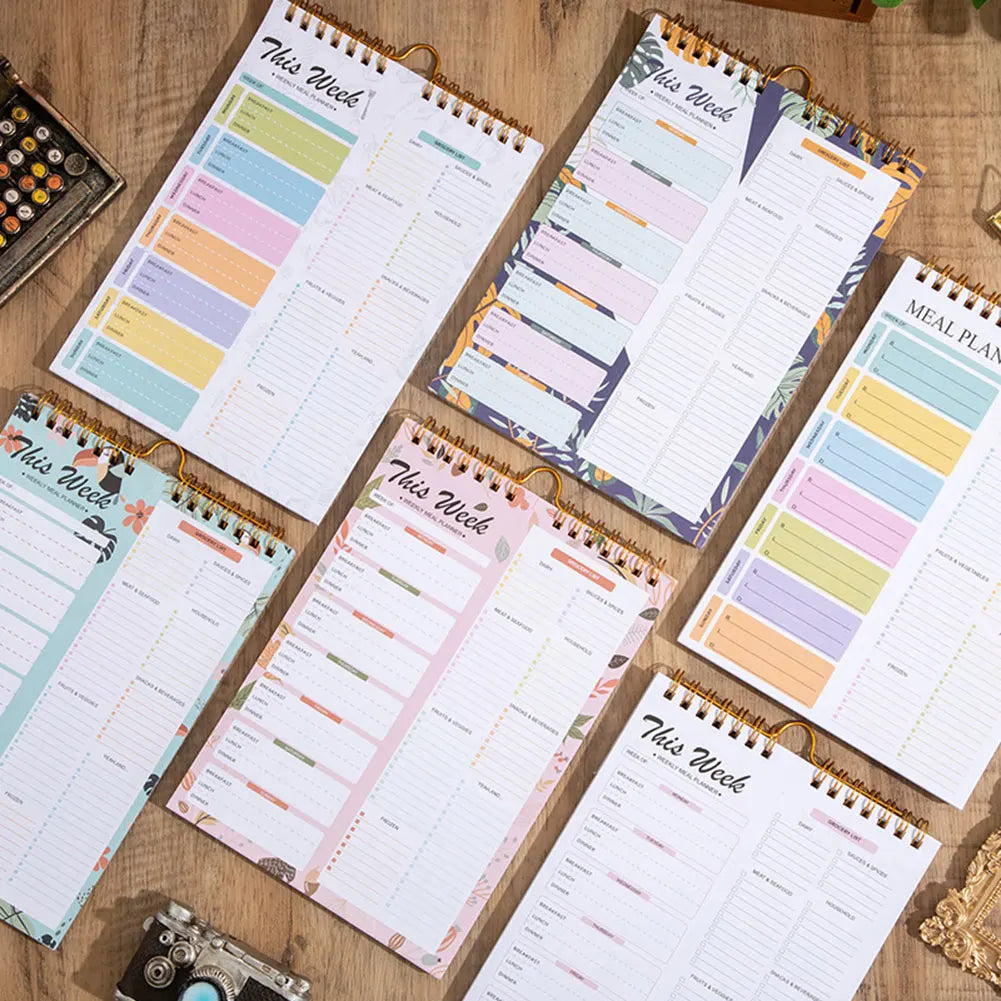 A collection of weekly meal planner and grocery list pads with printed schedules and blank lines on a wooden surface.