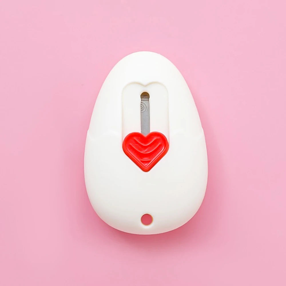 Navaja multiusos blanca con botón en forma de corazón rojo y hoja plateada sobre fondo rosa.