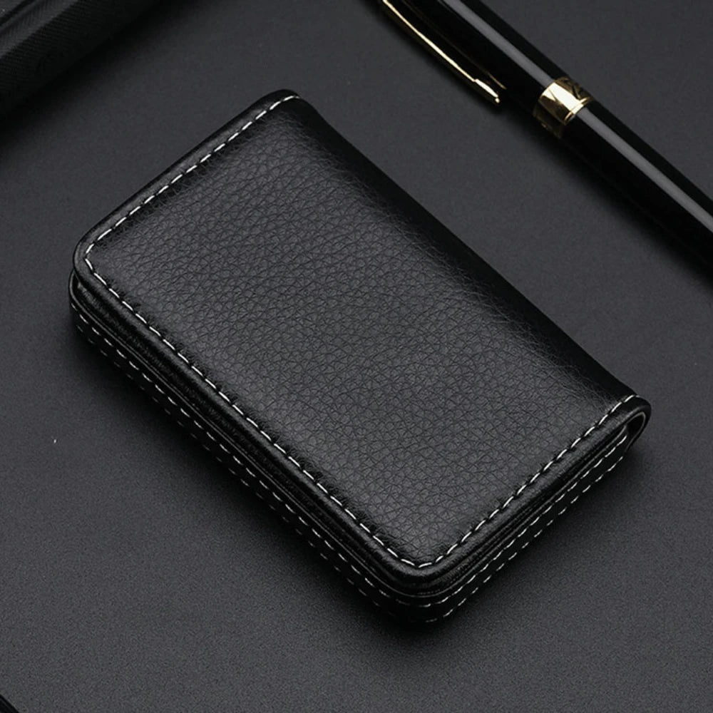 Cartera de cuero sintético negro cosida sobre una superficie oscura junto a un bolígrafo.