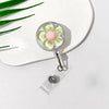 A clear plastic retractable ID badge holder with a floral pull buckle and a pink flower charm resting on a white plate.