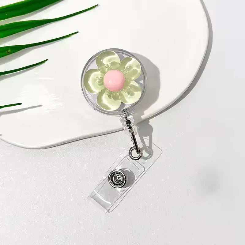 A clear plastic retractable ID badge holder with a floral pull buckle and a pink flower charm resting on a white plate.