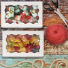 Two white boxes display colorful candies and cookies next to a ball of red yarn and scissors on a wooden surface.