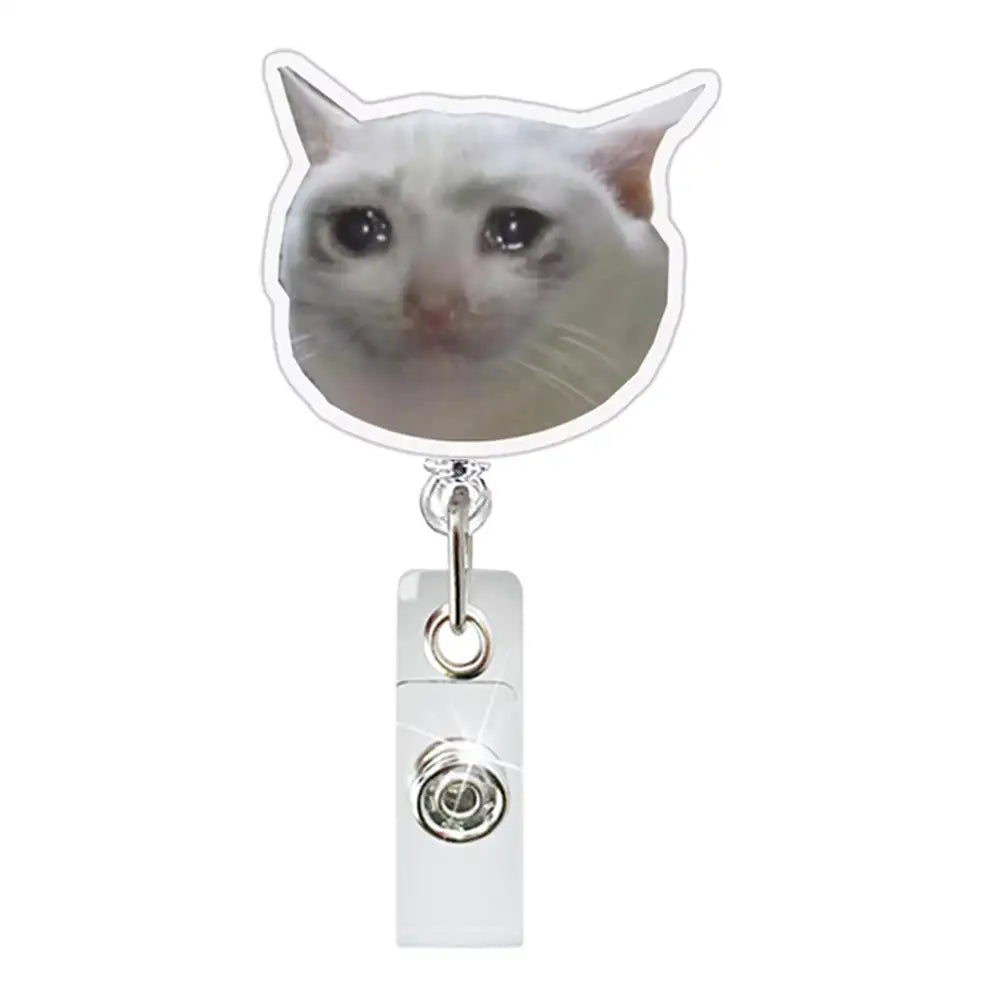 A silver retractable ID badge holder with a crocodile clip attached to a clear badge holder featuring a cat face charm.