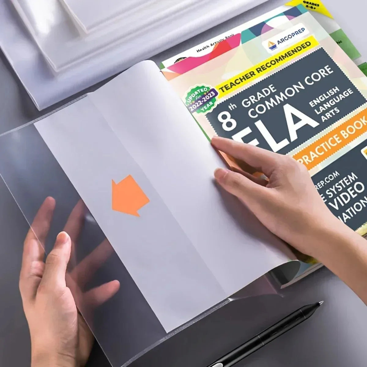 Una mano sostiene una cubierta protectora transparente abierta para documentos A4 y 16K con material educativo.