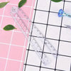 A set of precision folding transparent rulers and a blue glass tool are displayed on a pink and white grid background.
