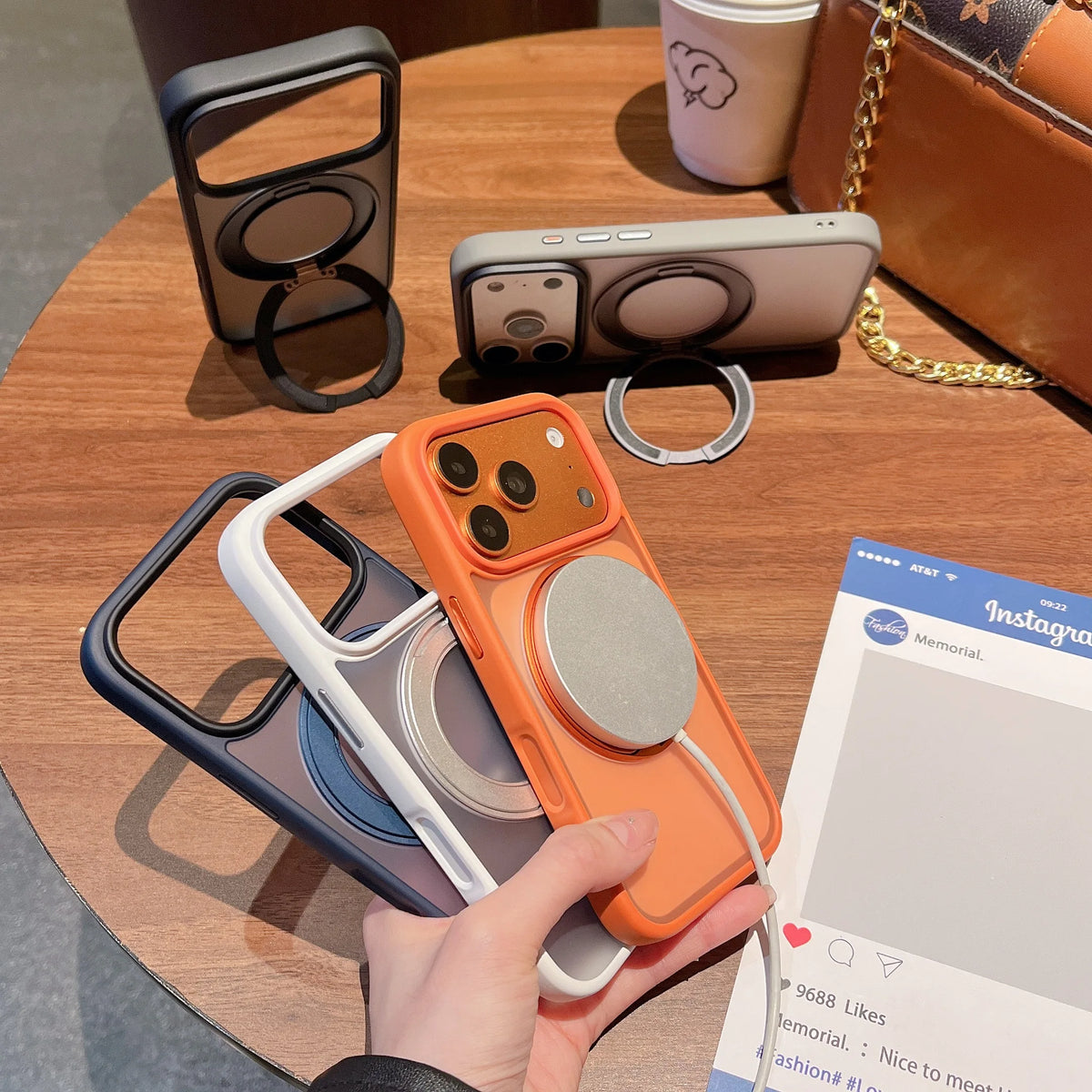 An orange phone case with a magnetic ring is held above a wooden table next to other accessories.