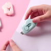 A hand holds a light blue portable utility knife against a pink piece of paper.