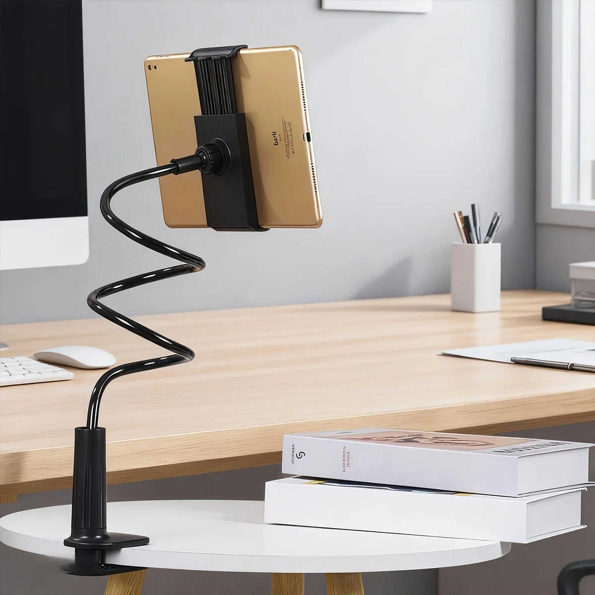 A gold-colored adjustable tablet and phone holder with a black stand, resting on a wooden desk.