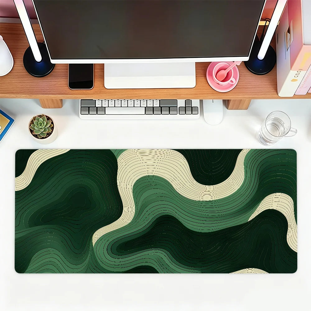 A dark green and beige abstract wave mouse pad placed on a wooden desk with a computer setup.