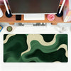 A dark green and beige abstract wave mouse pad placed on a wooden desk with a computer setup.