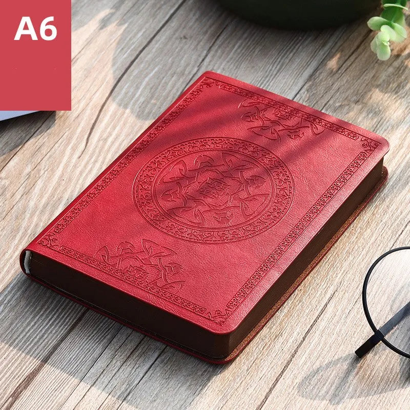 A red retro PU leather pocket notebook with embossed circular design lying on a wooden surface.