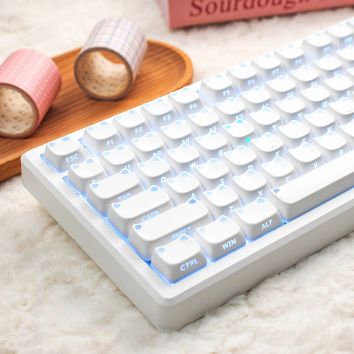 Nahaufnahme einer weißen mechanischen Tastatur mit hellblauen Tasten auf einer flauschigen Oberfläche neben rosa gerollten...