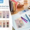 A collection of colorful sticky note tabs and pads displayed on a wooden table next to a notebook and pens.