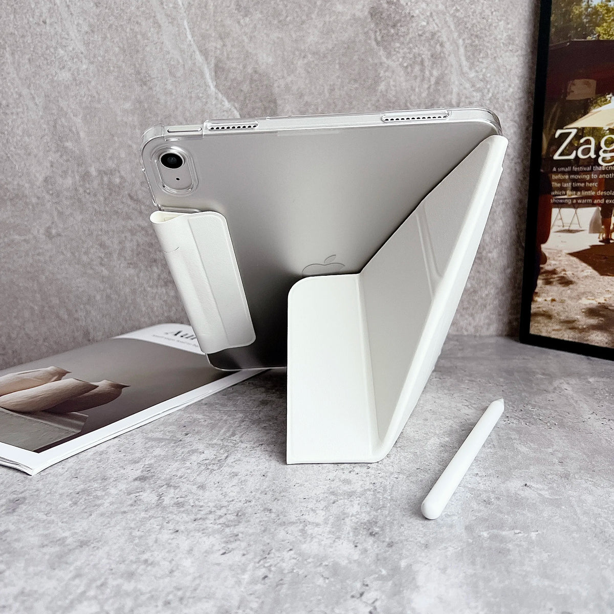 Un iPad Apple plateado con una funda protectora blanca y lápiz óptico sobre una superficie gris.