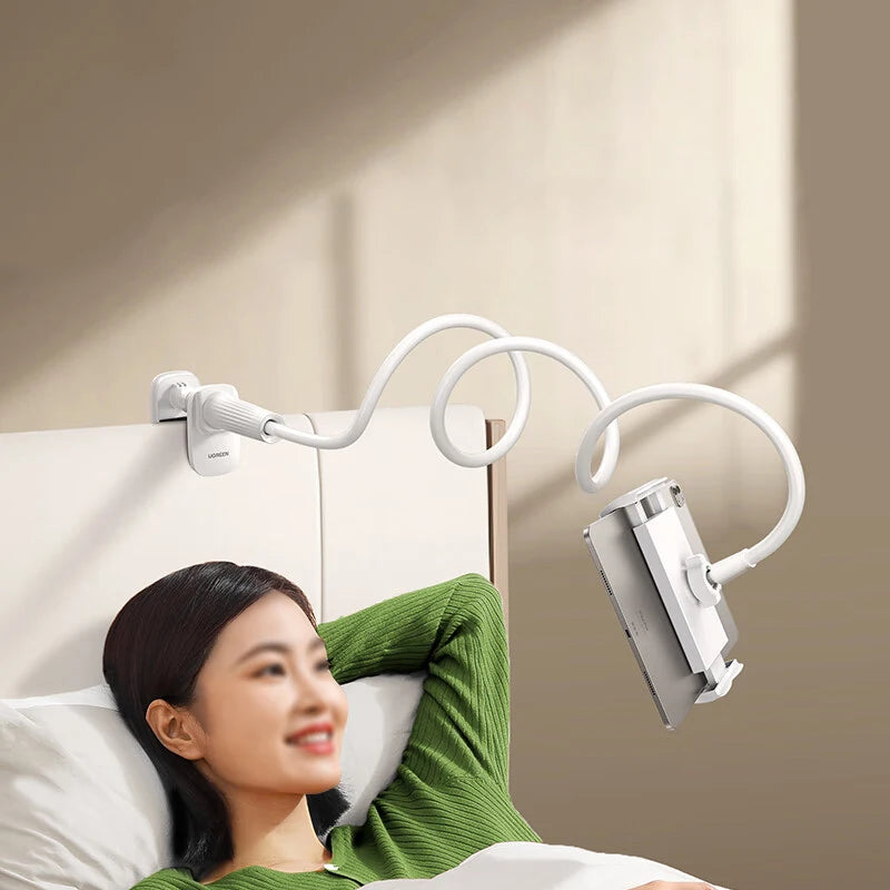 A woman is using a gooseneck tablet holder with a flexible arm mounted on a bedside surface.