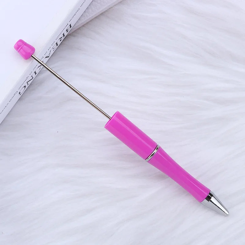 A pink DIY beadable pen with a silver tip and purple cap resting on a white, fluffy surface.