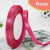 Roll of bright pink satin ribbon with gold edge, shown against a blurred background.