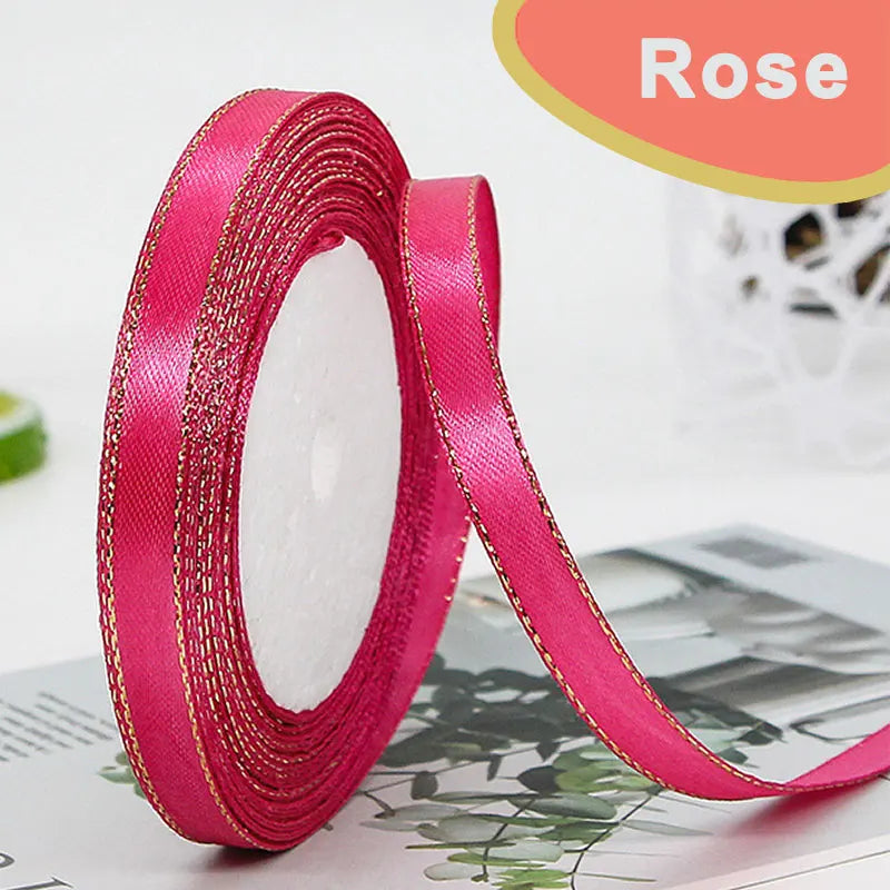 Roll of bright pink satin ribbon with gold edge, shown against a blurred background.