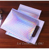 Rainbow foil bubble mailers stacked on a wooden surface.