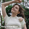 A woman wearing a white shirt and a beige clip-on fan for weightless wear in an outdoor setting.
