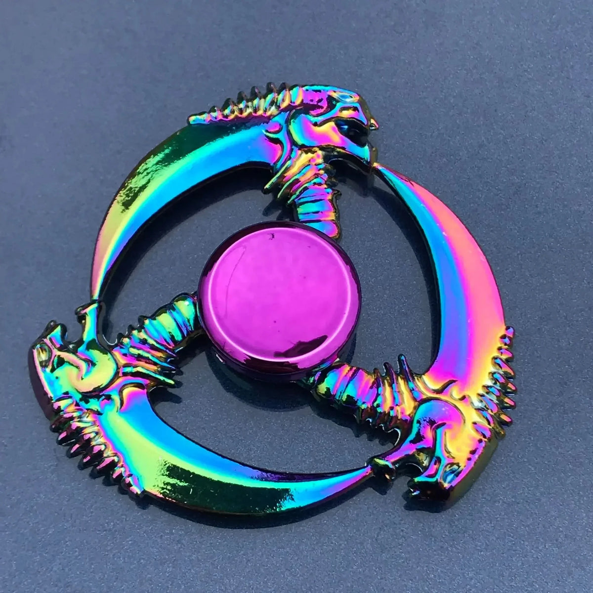 A rainbow metal fidget spinner with a dragon design, featuring iridescent colors and a central disc.