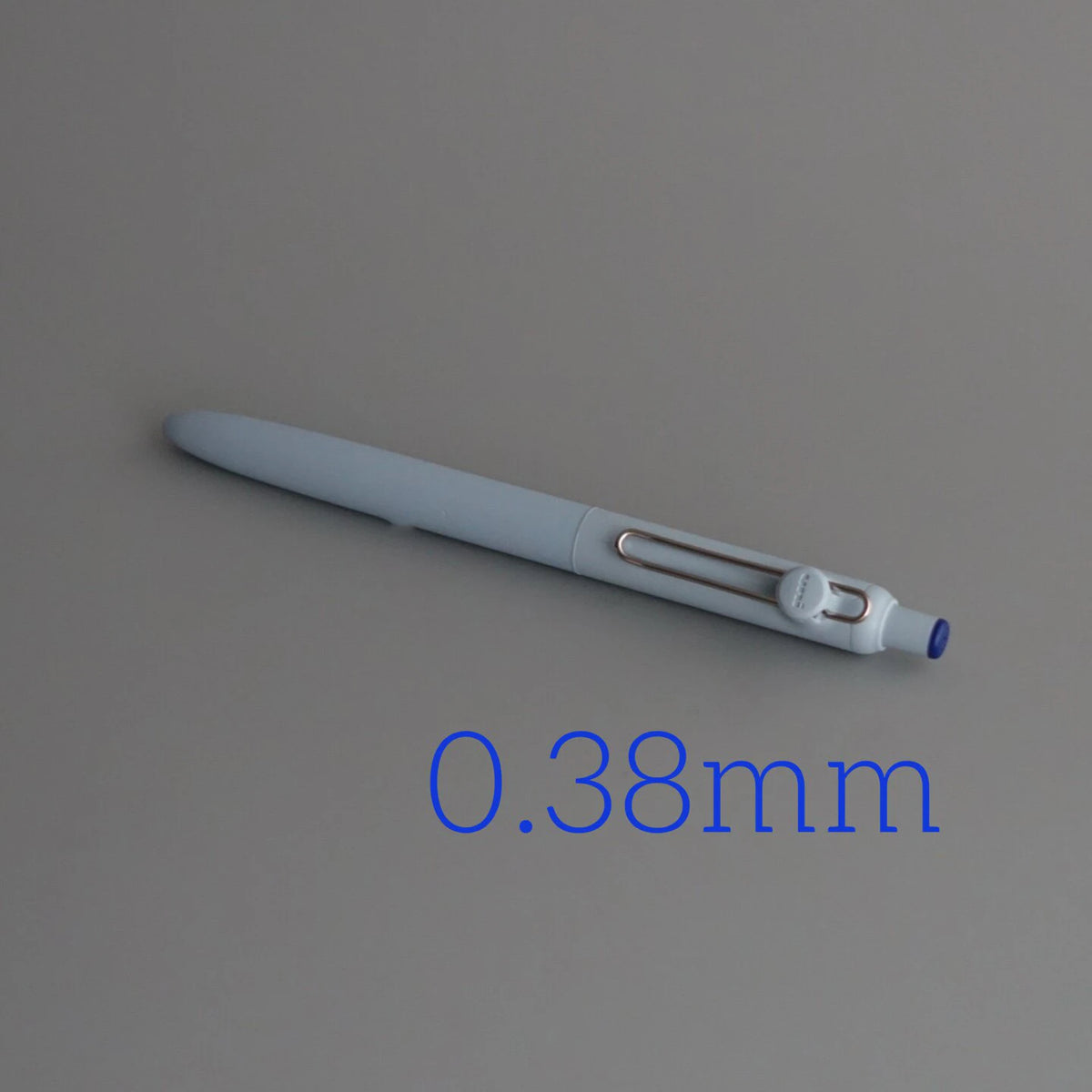 A close-up view of a light gray precision gel pen with a 0.38mm tip.