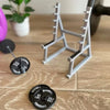 A gray metal barbell rack stands on a wooden desk next to a black barbell weight.