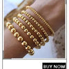 A close-up of a hand wearing multiple strands of gold-plated shell pearl beaded bracelets.