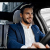 A man in a blue blazer is driving, holding the steering wheel of a car with a Bluetooth 5.3 Car Audio Adapter.