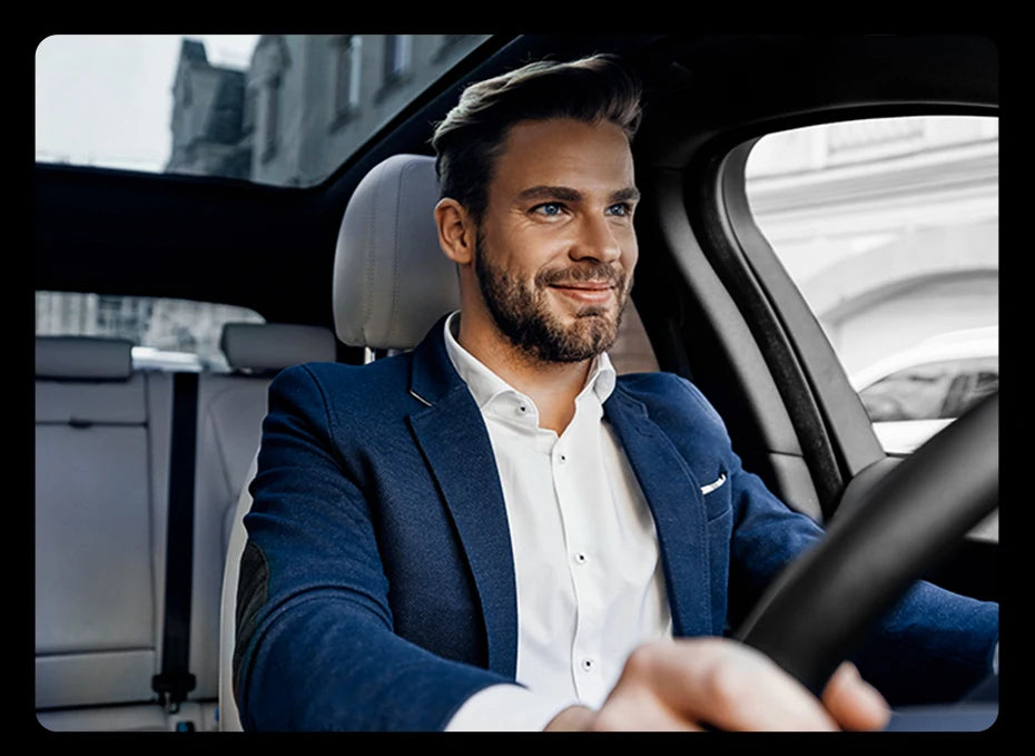 A man in a blue blazer is driving, holding the steering wheel of a car with a Bluetooth 5.3 Car Audio Adapter.