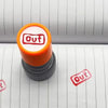 An orange rubber stamp with a red 'out' design is placed on lined paper.