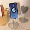 A black smartphone is mounted on an adjustable desktop stand, displaying a music player interface.