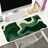 A dark green mouse pad with abstract wavy patterns is displayed on a white desk next to a computer and stationery.