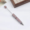 A silver pen accessory featuring a rhinestone-encrusted tip and decorative bead on a slender metal shaft.