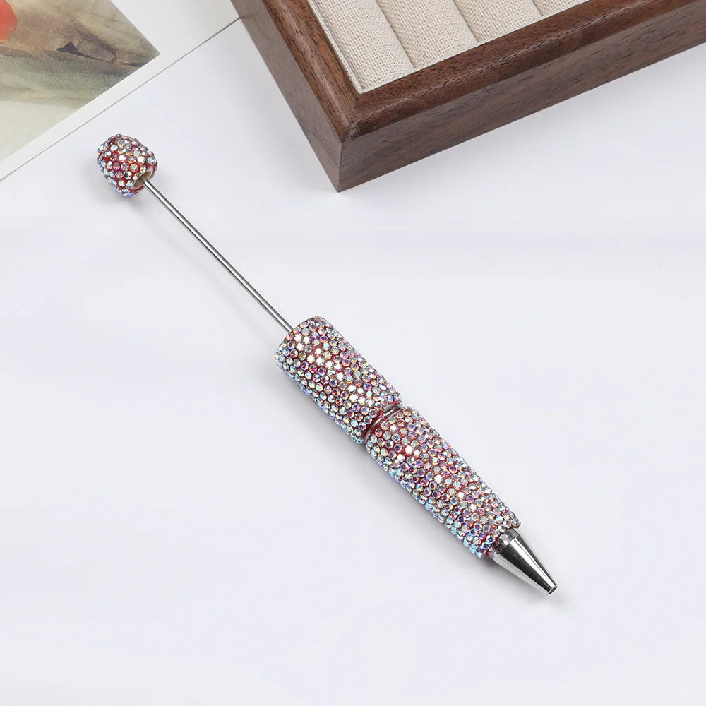 A silver pen accessory featuring a rhinestone-encrusted tip and decorative bead on a slender metal shaft.
