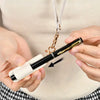 A person holds a gold-colored leather pen holder keychain with a black pen inside against a light beige top.