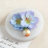 A light blue and purple flower arrangement displayed on a white circular card.