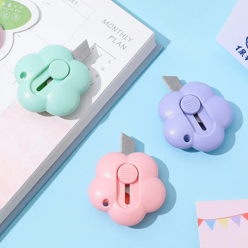 A set of three plastic floral design letter openers and paper cutters in mint green, lavender, and pink on a light blue backg